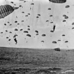 Paraquedistas aliados saltando sobre a Holanda durante a Operação Market Garden em 17 de setembro de 1944, com aeronaves C-47 ao fundo.